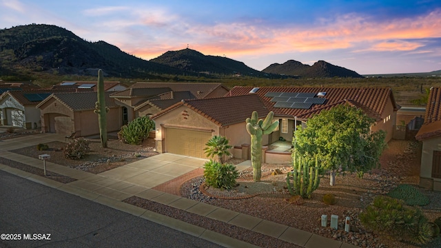 view of front facade with an attached garage, a mountain view, a tile roof, concrete driveway, and stucco siding