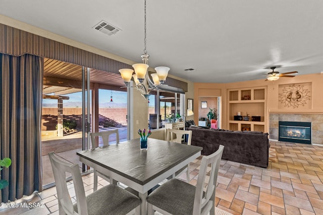 dining space featuring a fireplace, visible vents, built in features, and ceiling fan with notable chandelier