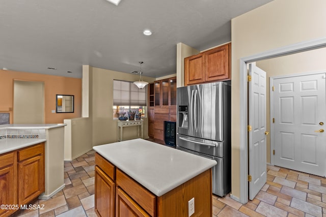 kitchen with stone tile floors, brown cabinets, a center island, light countertops, and stainless steel refrigerator with ice dispenser