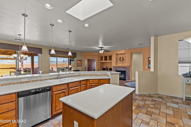 kitchen featuring light countertops, stainless steel dishwasher, stone finish floor, a sink, and a lit fireplace