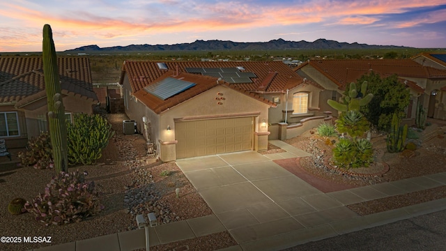 view of front of house with a mountain view, a garage, a tiled roof, roof mounted solar panels, and stucco siding