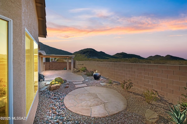 yard at dusk with a patio area, a fenced backyard, and a mountain view