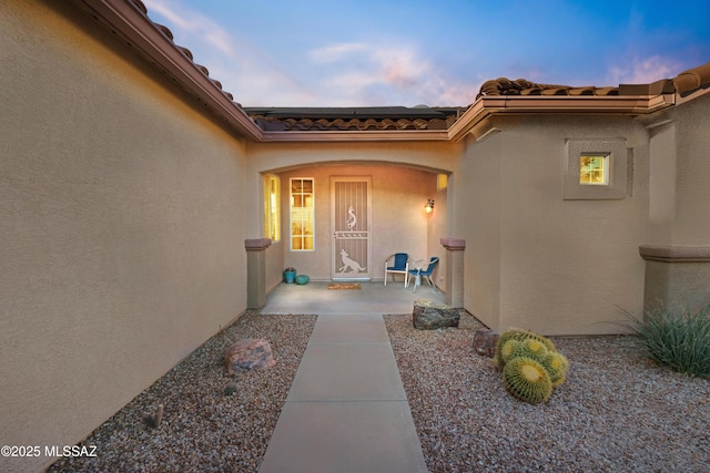 exterior entry at dusk with a patio area and stucco siding