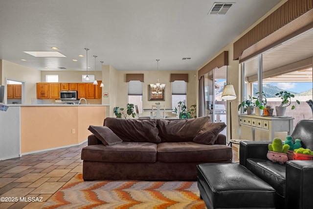 living room featuring a skylight, stone tile floors, recessed lighting, visible vents, and a chandelier