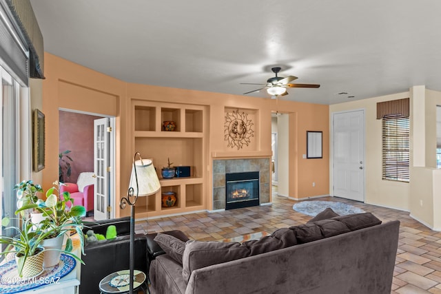 living area featuring baseboards, ceiling fan, stone finish flooring, built in shelves, and a fireplace