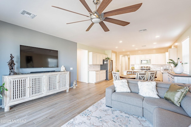 living room with light wood-type flooring, ceiling fan, visible vents, and recessed lighting