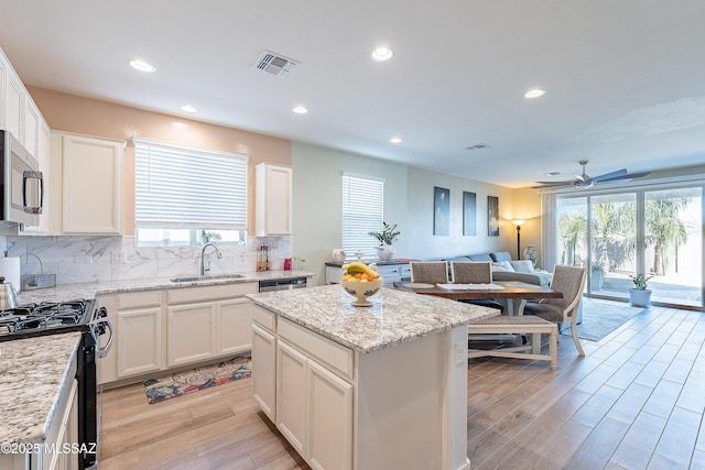 kitchen featuring visible vents, decorative backsplash, stainless steel microwave, black range with gas stovetop, and a sink