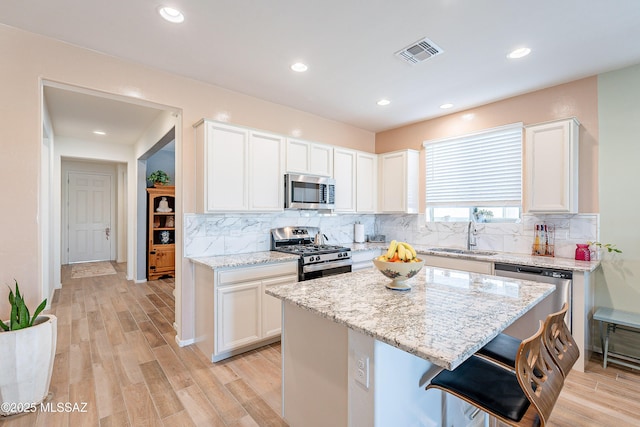 kitchen with visible vents, light stone countertops, stainless steel appliances, light wood-style floors, and a sink