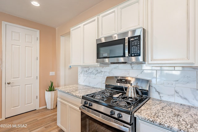 kitchen featuring appliances with stainless steel finishes, light stone countertops, light wood-style flooring, and decorative backsplash