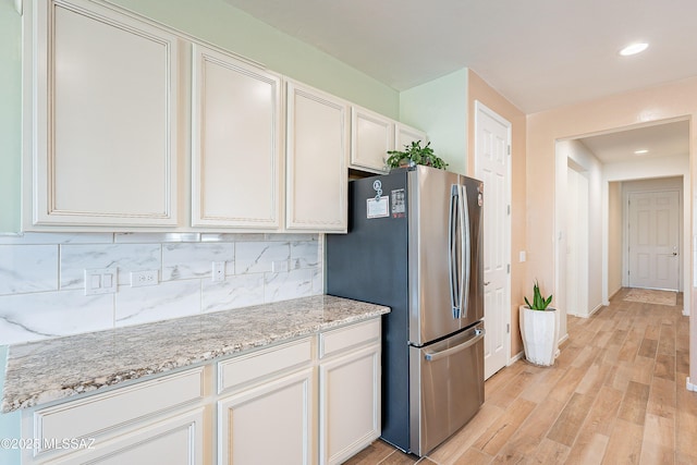 kitchen featuring backsplash, light wood-style floors, freestanding refrigerator, white cabinetry, and light stone countertops