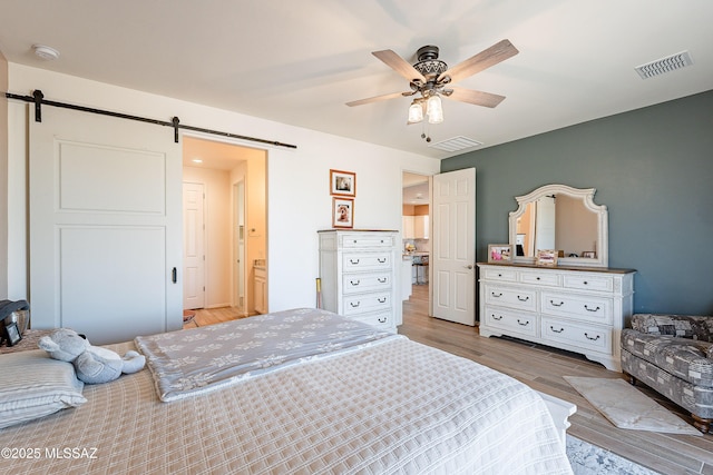 bedroom featuring a barn door, visible vents, and light wood-style floors