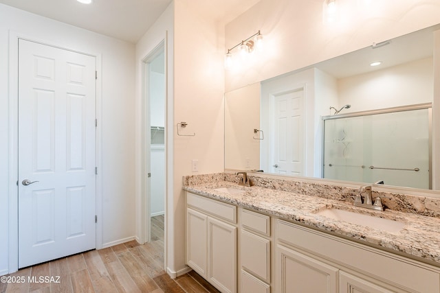 full bath with double vanity, a shower stall, a sink, and wood finished floors