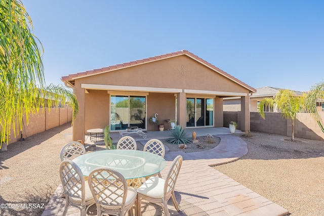 rear view of house featuring a patio, outdoor dining area, a fenced backyard, and stucco siding