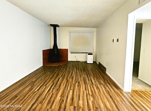 unfurnished living room featuring a wood stove, a textured ceiling, baseboards, and wood finished floors