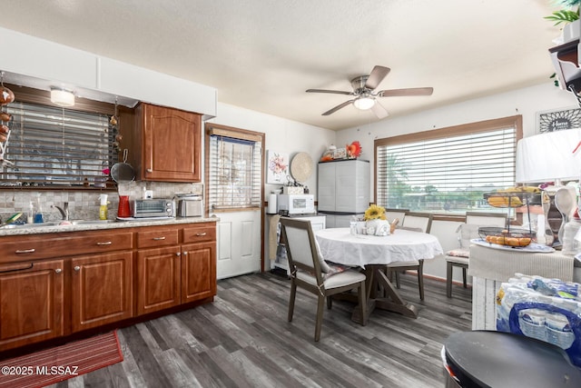 kitchen with dark wood-style flooring, brown cabinets, tasteful backsplash, white microwave, and a sink