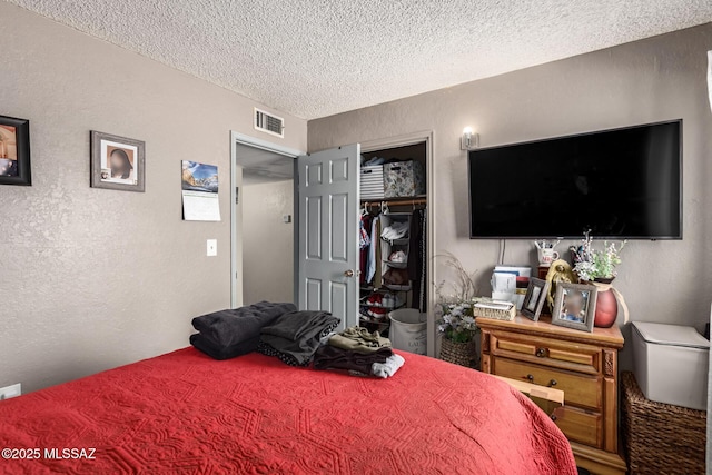 bedroom with a closet, visible vents, a textured ceiling, and a textured wall