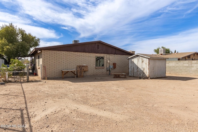 rear view of property featuring brick siding, an outdoor structure, a storage shed, and fence