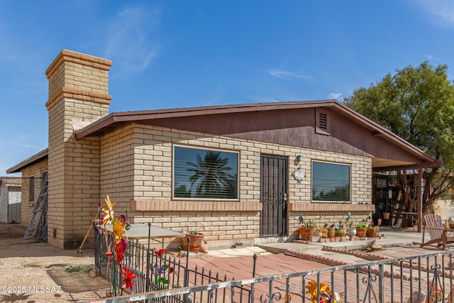 view of front of house with brick siding, a chimney, and fence