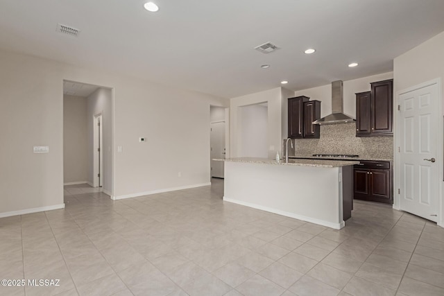 kitchen with decorative backsplash, visible vents, an island with sink, and wall chimney exhaust hood