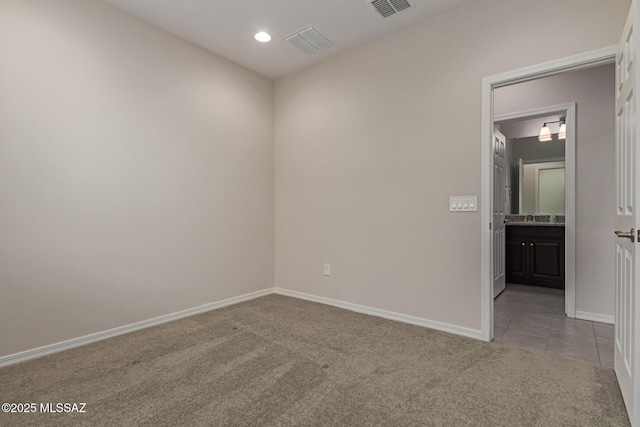 tiled spare room with carpet floors, visible vents, a sink, and baseboards