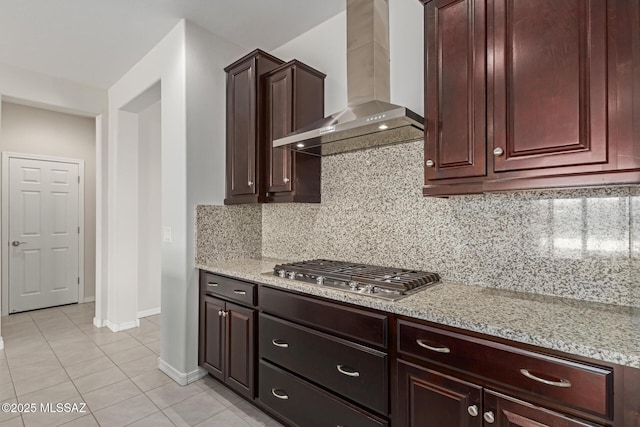 kitchen featuring light tile patterned floors, stainless steel gas cooktop, wall chimney range hood, decorative backsplash, and light stone countertops