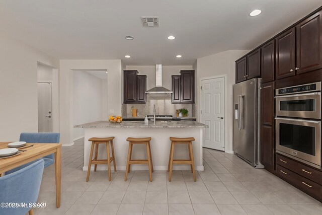 kitchen featuring visible vents, a kitchen breakfast bar, appliances with stainless steel finishes, wall chimney range hood, and backsplash