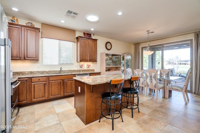 kitchen featuring a breakfast bar area, visible vents, brown cabinetry, a sink, and light stone countertops