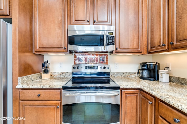 kitchen with stainless steel appliances, light stone counters, and brown cabinets