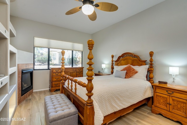 bedroom with baseboards, a fireplace, light wood-type flooring, and ceiling fan