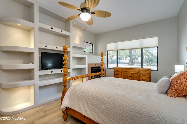 bedroom featuring a tiled fireplace, wood finished floors, and a ceiling fan