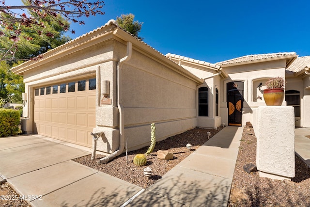 view of side of home featuring stucco siding, a tiled roof, concrete driveway, and a garage