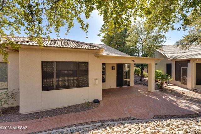 back of property with stucco siding, a patio, and a tile roof