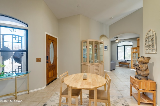 dining space with light tile patterned floors, a ceiling fan, arched walkways, and high vaulted ceiling