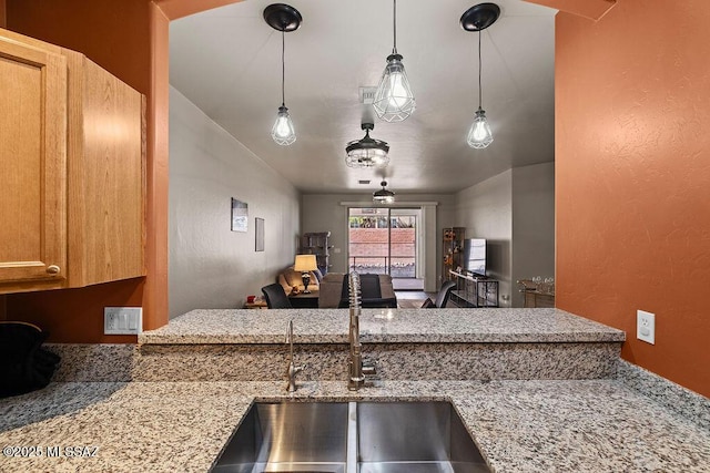 kitchen with a sink, open floor plan, light stone counters, a textured wall, and decorative light fixtures