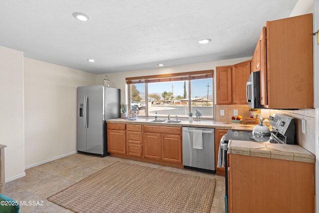 kitchen with tile counters, recessed lighting, decorative backsplash, appliances with stainless steel finishes, and a sink