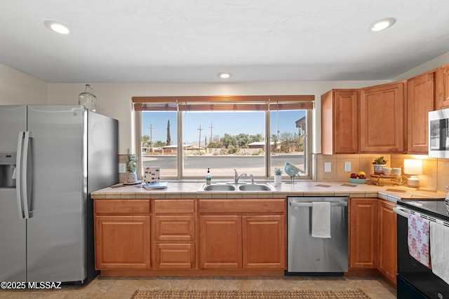 kitchen with tile countertops, appliances with stainless steel finishes, backsplash, and a sink