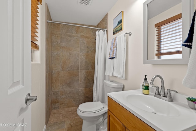 full bathroom with toilet, vanity, a tile shower, and visible vents