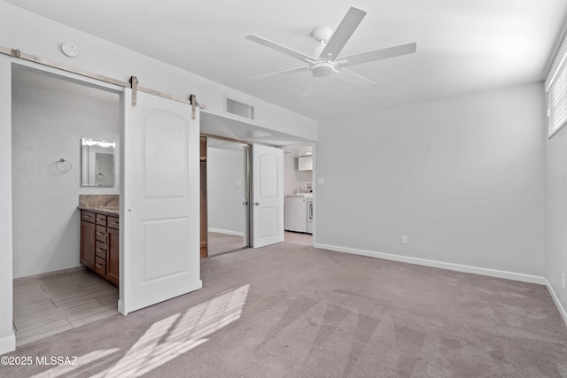 unfurnished bedroom with light carpet, a barn door, visible vents, connected bathroom, and independent washer and dryer