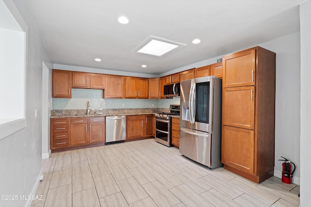 kitchen featuring light stone counters, brown cabinets, recessed lighting, appliances with stainless steel finishes, and a sink