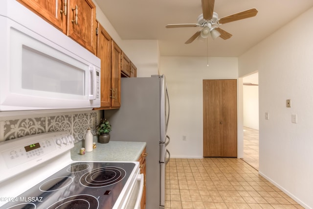 kitchen featuring light countertops, brown cabinetry, a ceiling fan, white appliances, and baseboards