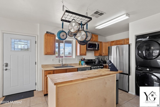 kitchen featuring stainless steel appliances, a sink, visible vents, stacked washer / drying machine, and wooden counters