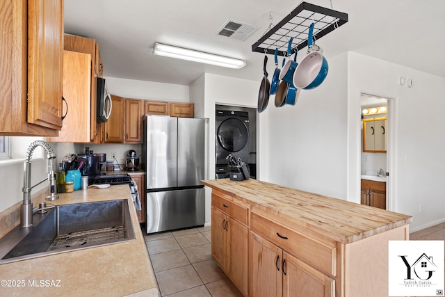 kitchen with stainless steel appliances, visible vents, a sink, wood counters, and stacked washing maching and dryer