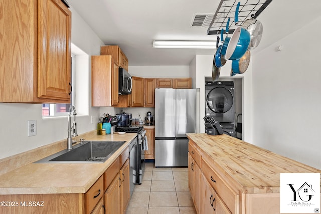 kitchen featuring light tile patterned floors, stacked washer / dryer, appliances with stainless steel finishes, wooden counters, and a sink