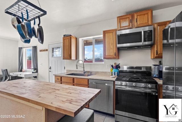 kitchen with butcher block counters, appliances with stainless steel finishes, brown cabinetry, light tile patterned flooring, and a sink