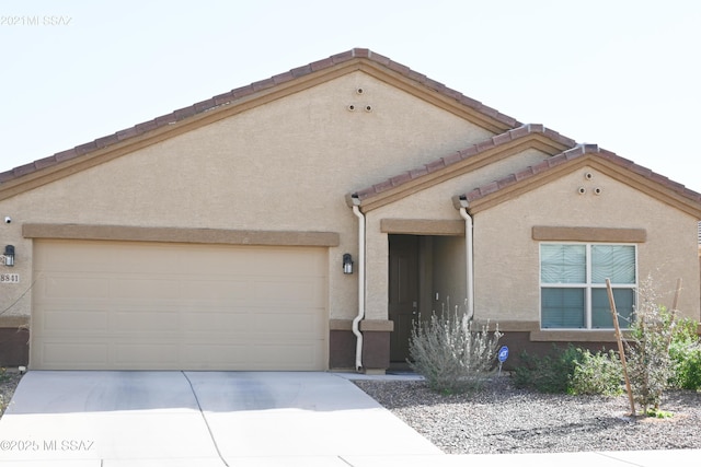 view of front of house with driveway, a tile roof, a garage, and stucco siding