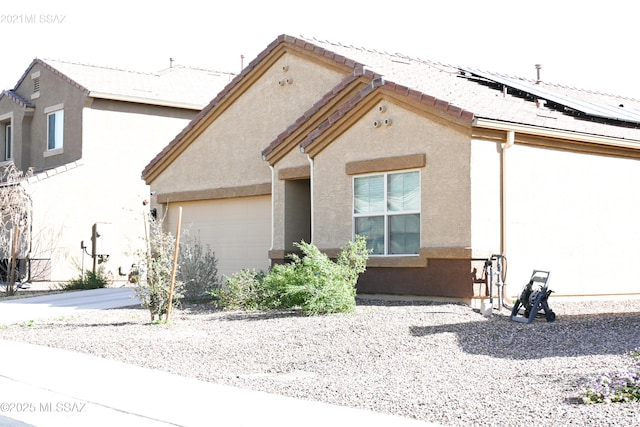 view of front of property featuring a tiled roof, an attached garage, roof mounted solar panels, and stucco siding