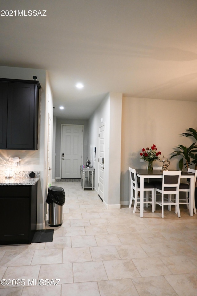 kitchen featuring baseboards, light stone counters, dark cabinets, and recessed lighting