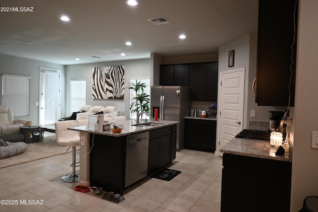 kitchen featuring light stone counters, recessed lighting, a sink, open floor plan, and appliances with stainless steel finishes