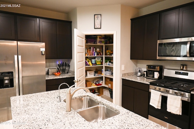 kitchen featuring appliances with stainless steel finishes, a sink, and light stone countertops