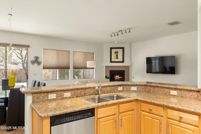 kitchen with open floor plan, light stone countertops, light brown cabinetry, stainless steel dishwasher, and a sink